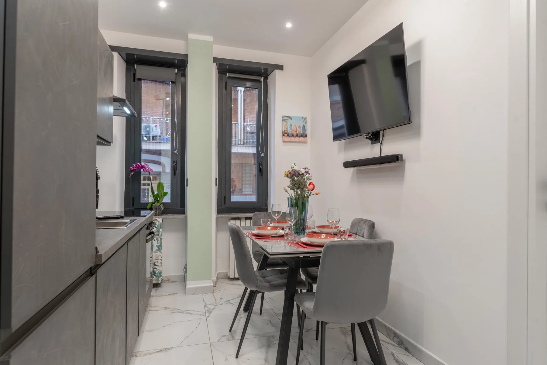 A compact dining area with a set table, gray seating, and a wall-mounted television.