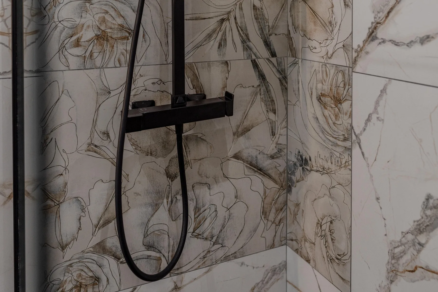 A shower with large floral-patterned wall tiles.