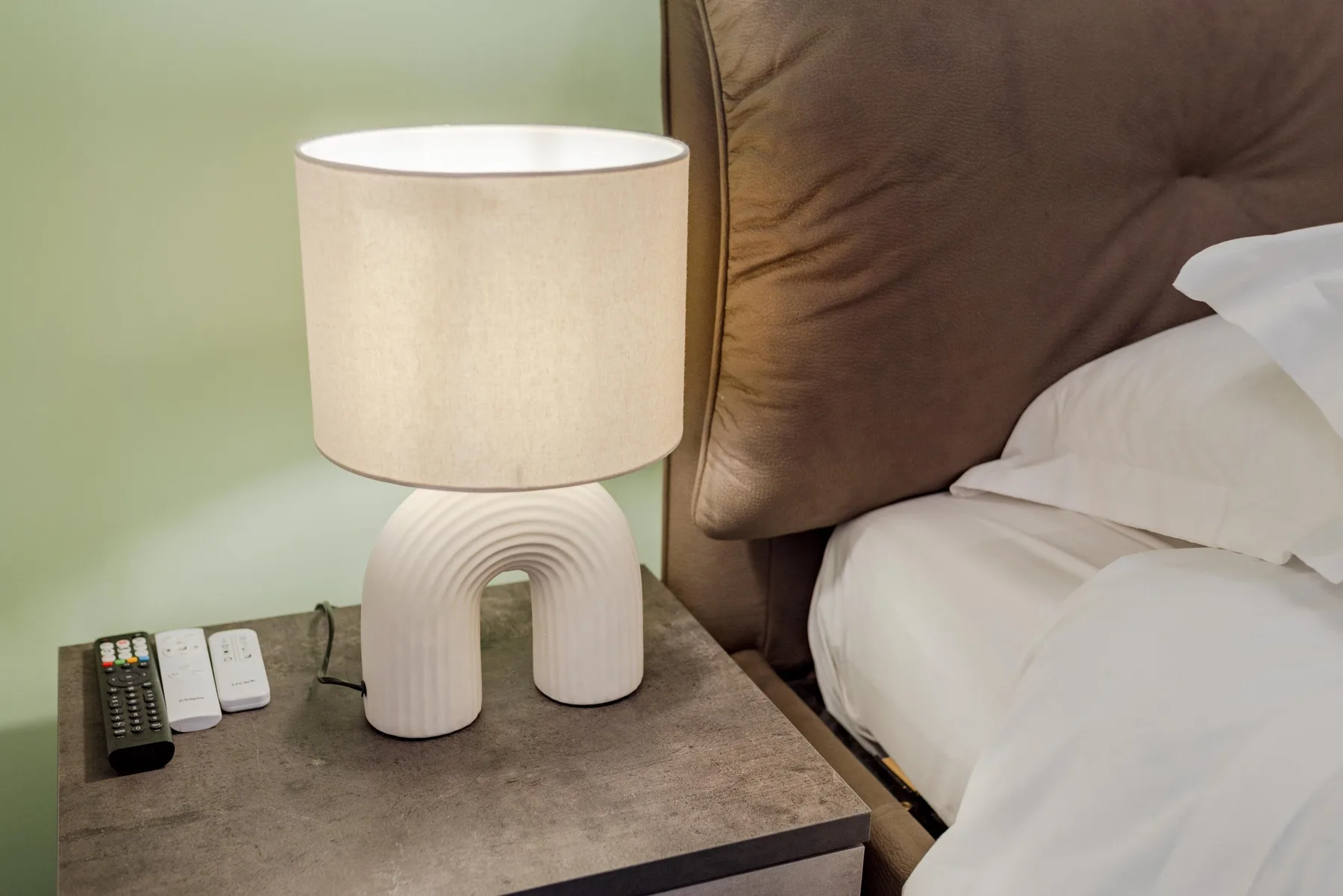 A bedside table holds a lamp and remotes beside a bed.