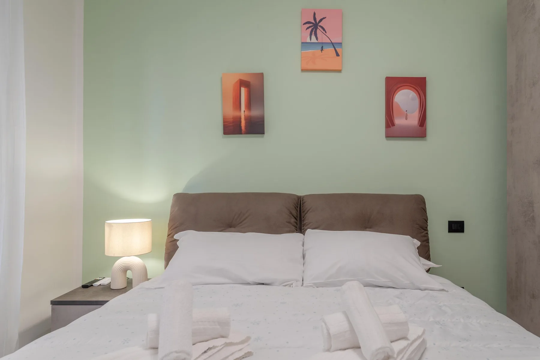 A bedroom with a neatly made bed, bedside table, and wall art.