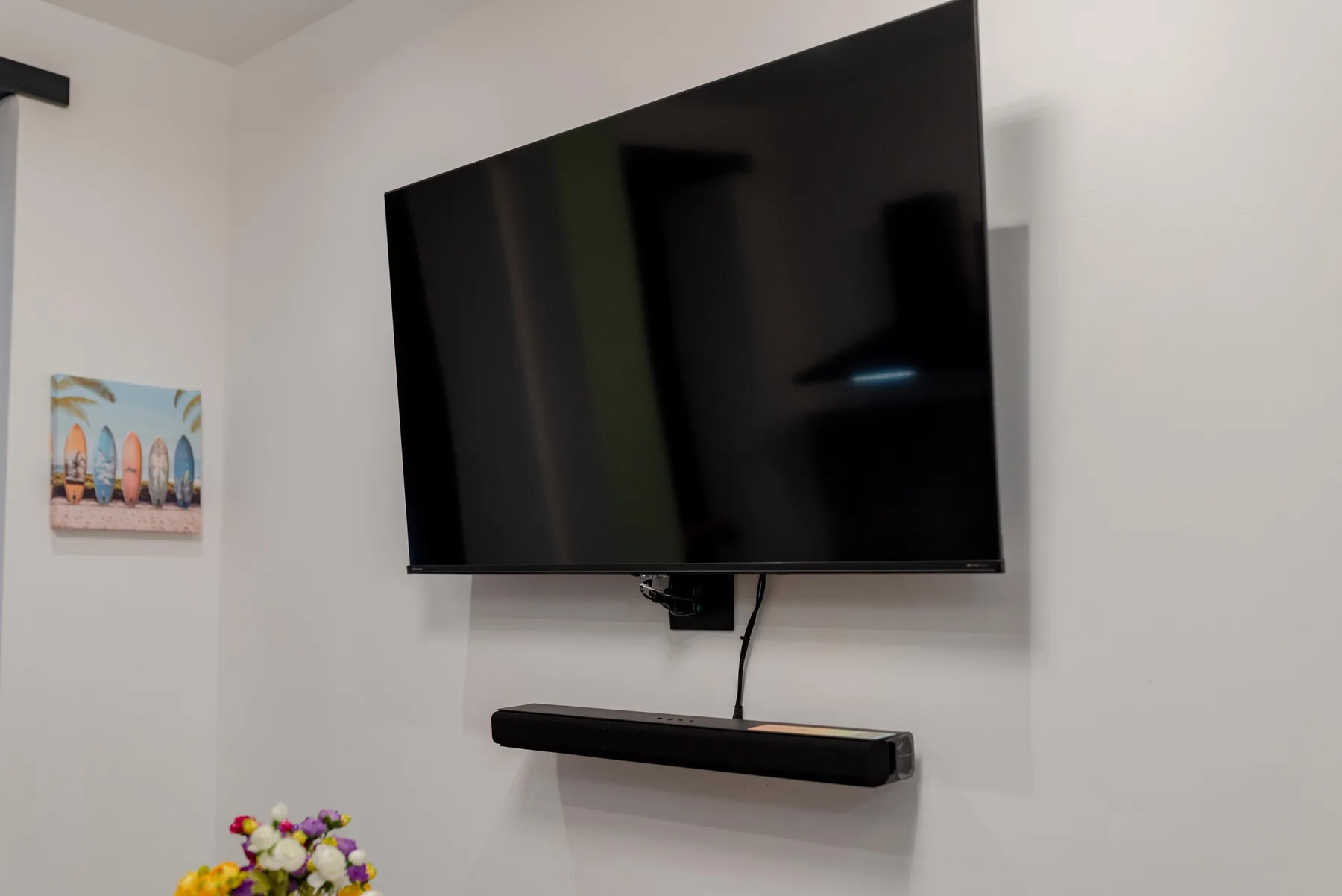 A wall-mounted television hangs above a narrow shelf in a bright room.