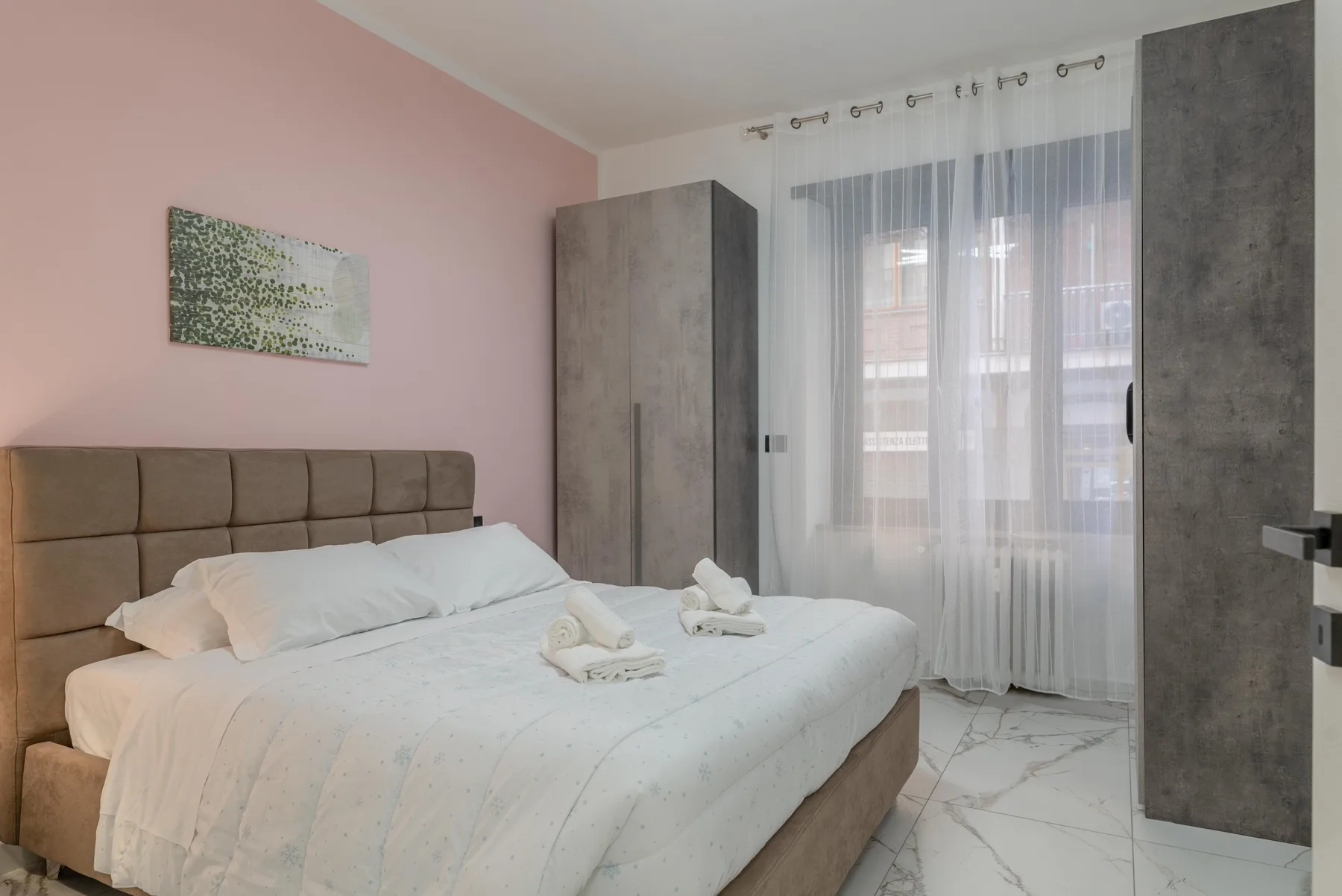 A bedroom with a double bed, bedside wardrobes, and a window with sheer curtains.
