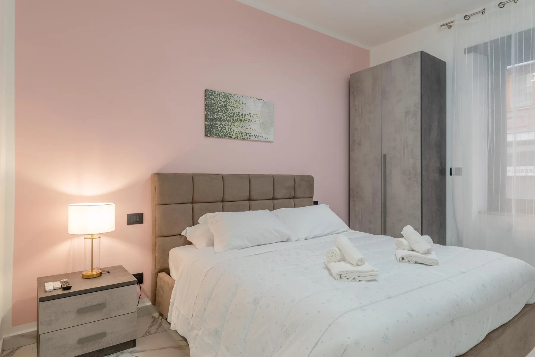 A bedroom with a neatly made bed, bedside table, and wardrobe.