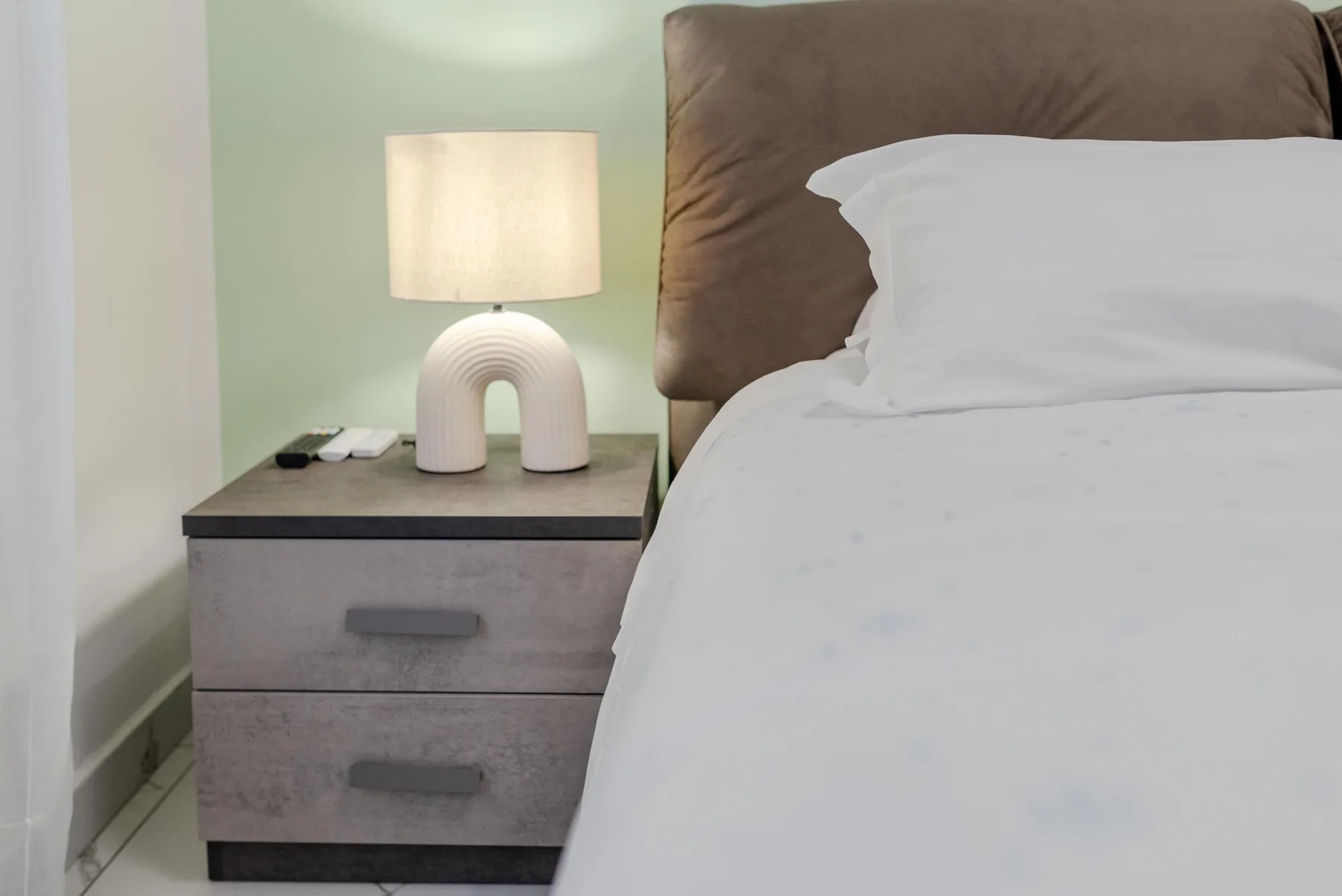 A bedroom with a bedside table, lamp, and neatly made bed.