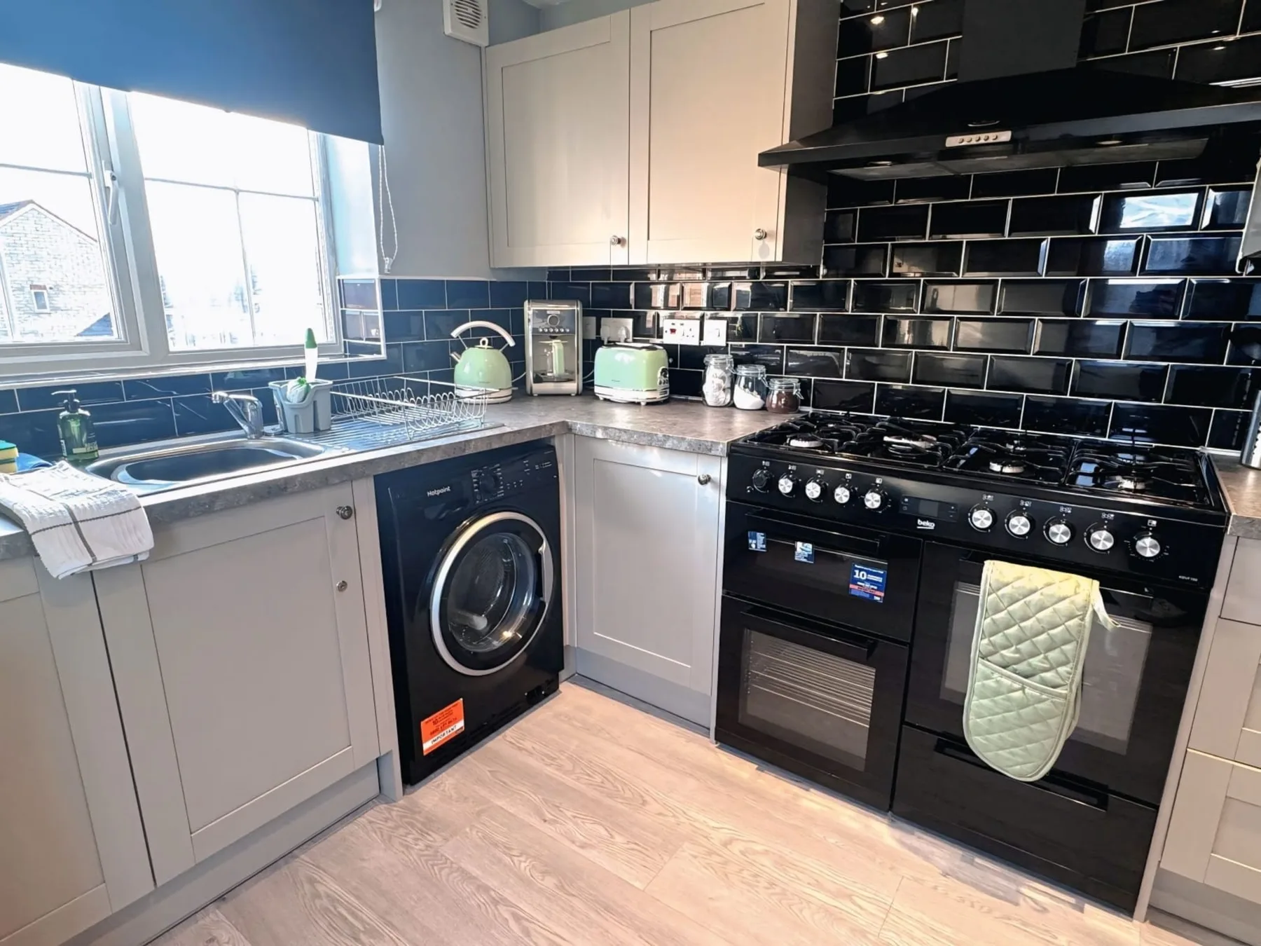 A bright kitchen with black tiled walls and a countertop beside the window.