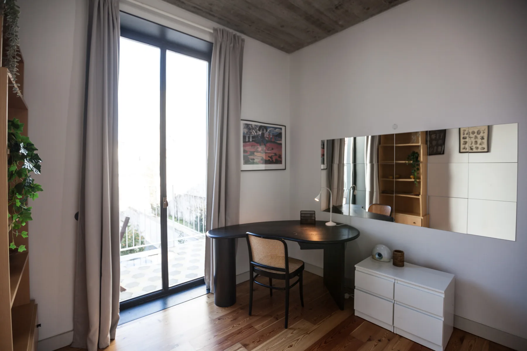 Una habitación luminosa con un escritorio junto a una ventana grande y un espejo de pared.