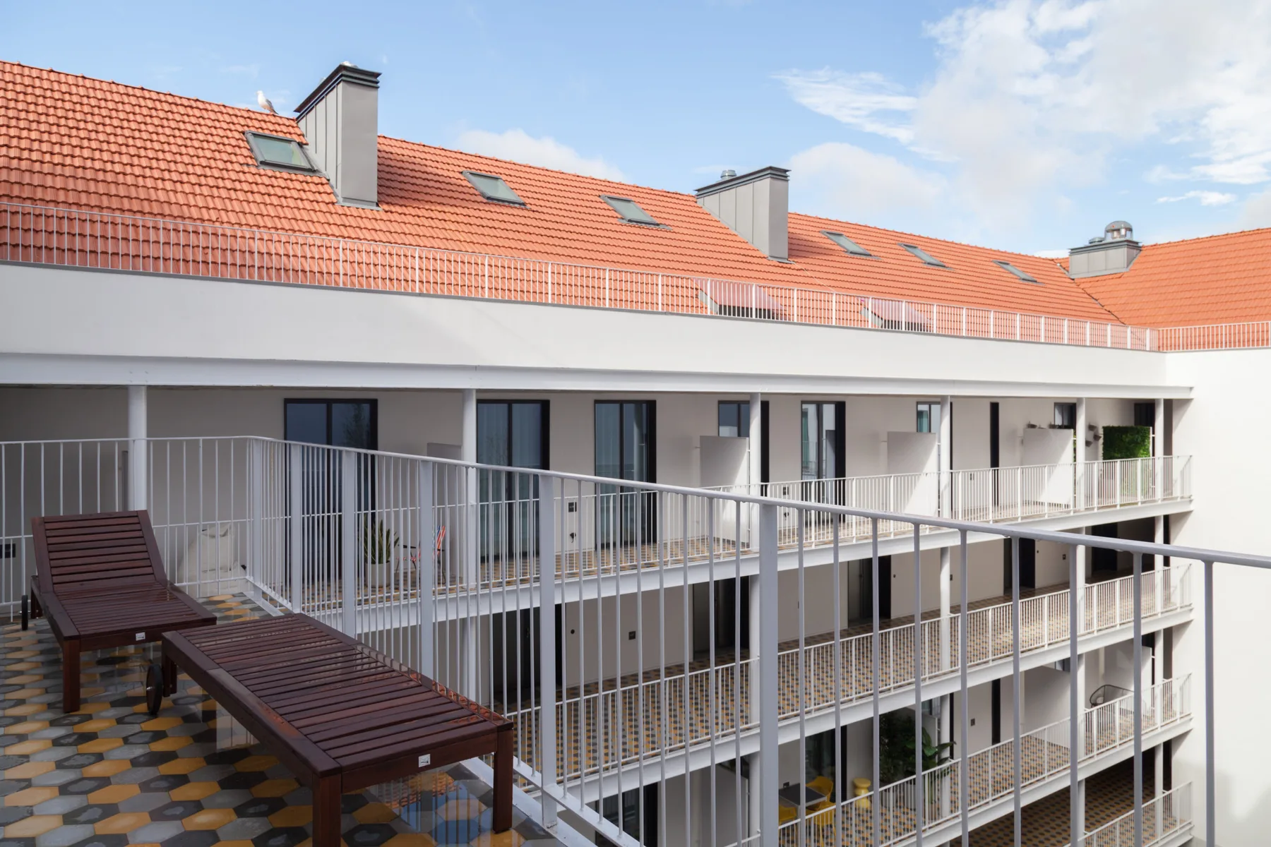 Edificio de apartamentos con balcones hacia un patio y un tejado de tejas rojas.