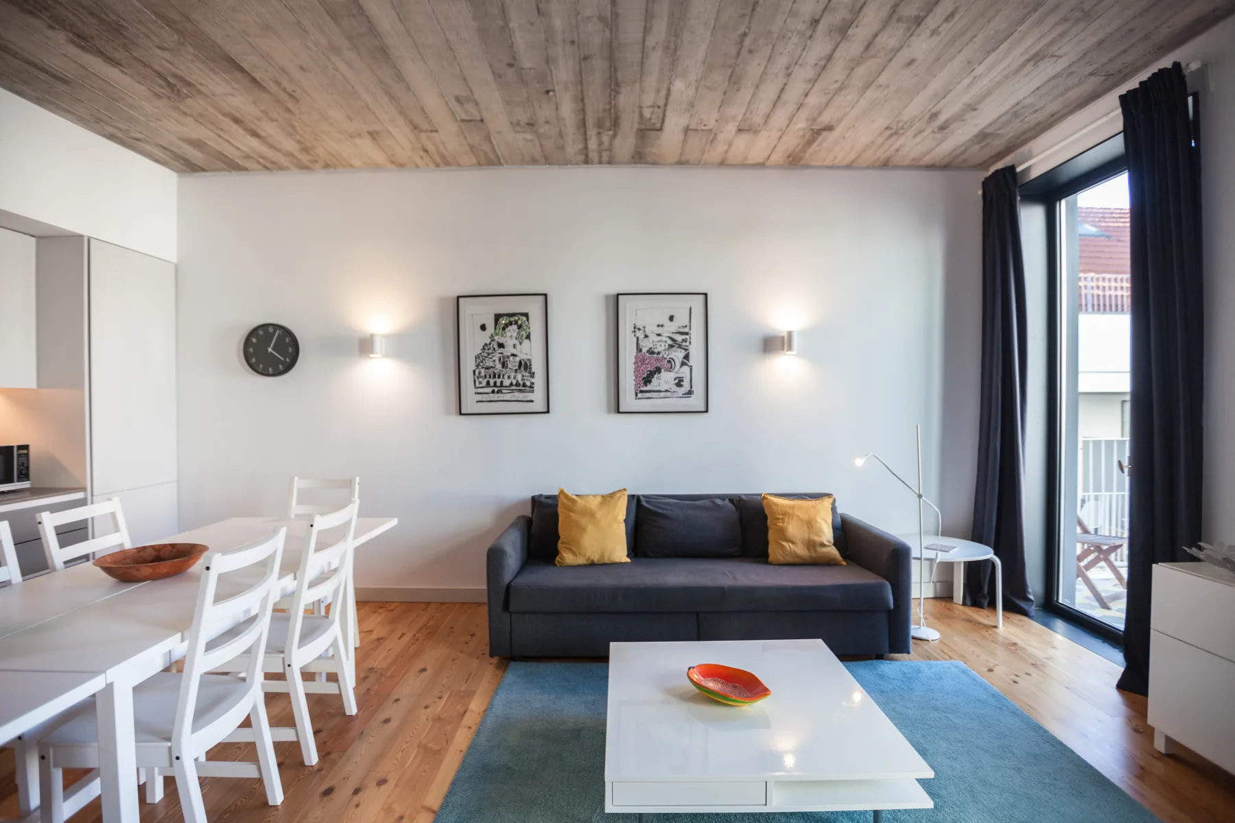 Sala de estar con sofá oscuro, mesa de comedor y ventanas grandes.