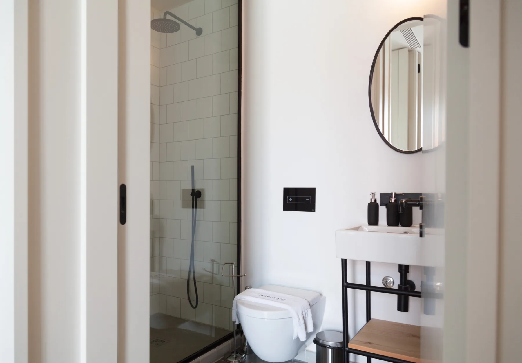 Un baño luminoso con ducha de cristal, lavabo y espejo ovalado.