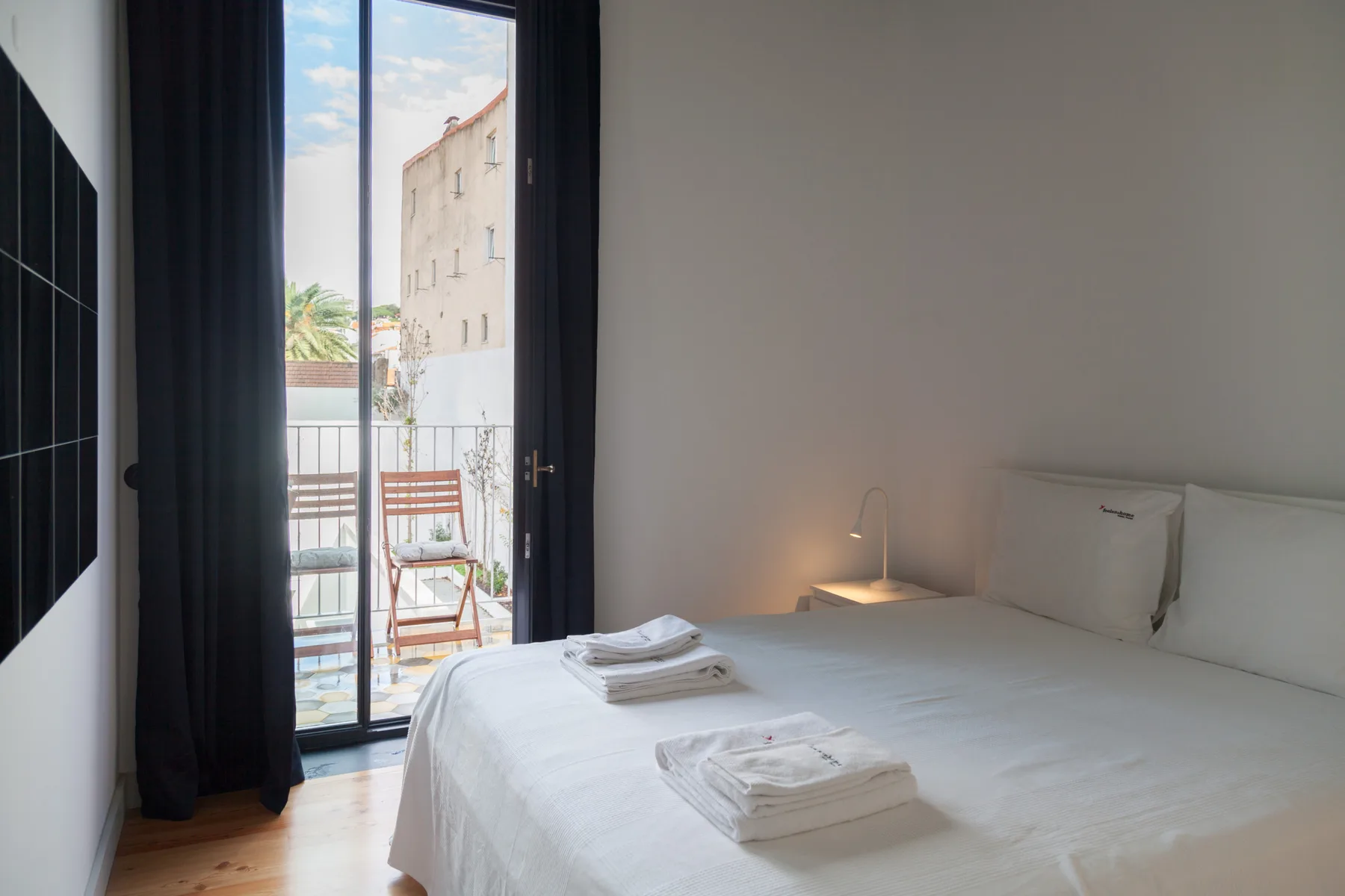 Un dormitorio con una cama bien hecha junto a una ventana alta con vistas a un balcón.