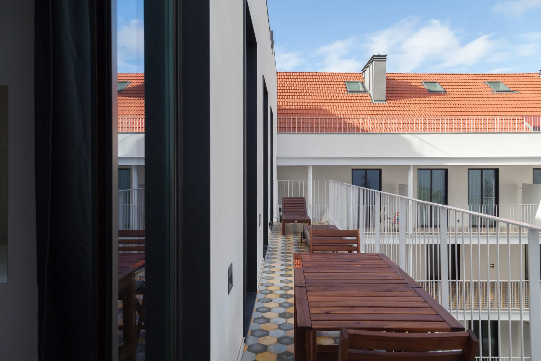 Un pasillo de balcón con asientos de madera da a un patio con ventanas.