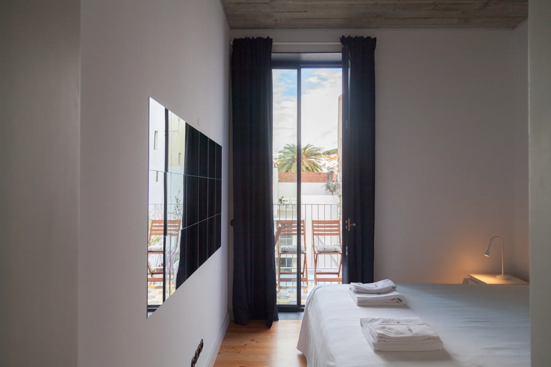 Un dormitorio con una cama junto a puertas de vidrio altas y cortinas oscuras.