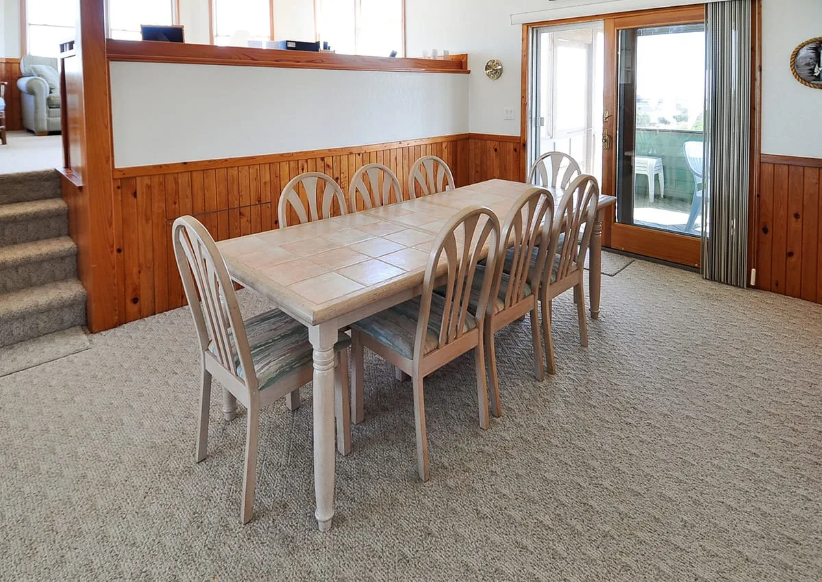A dining area with a rectangular table and chairs beside sliding glass doors.