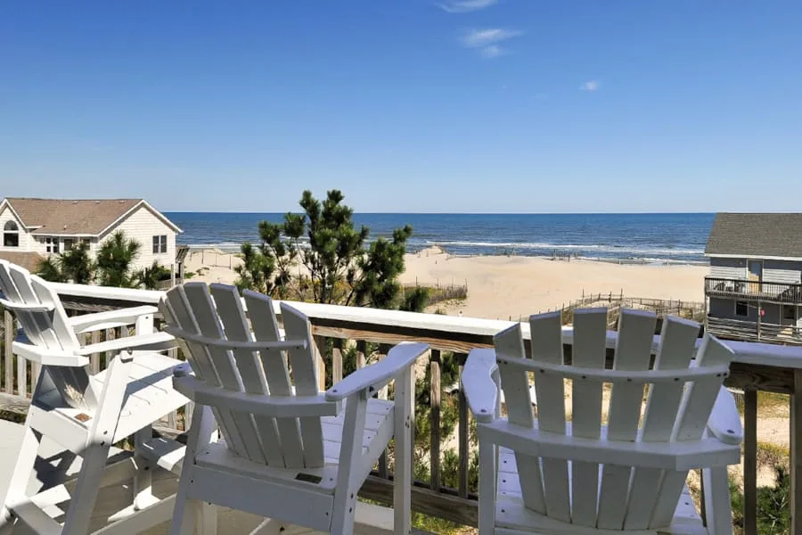 A seaside deck overlooks the beach and ocean, with outdoor seating.