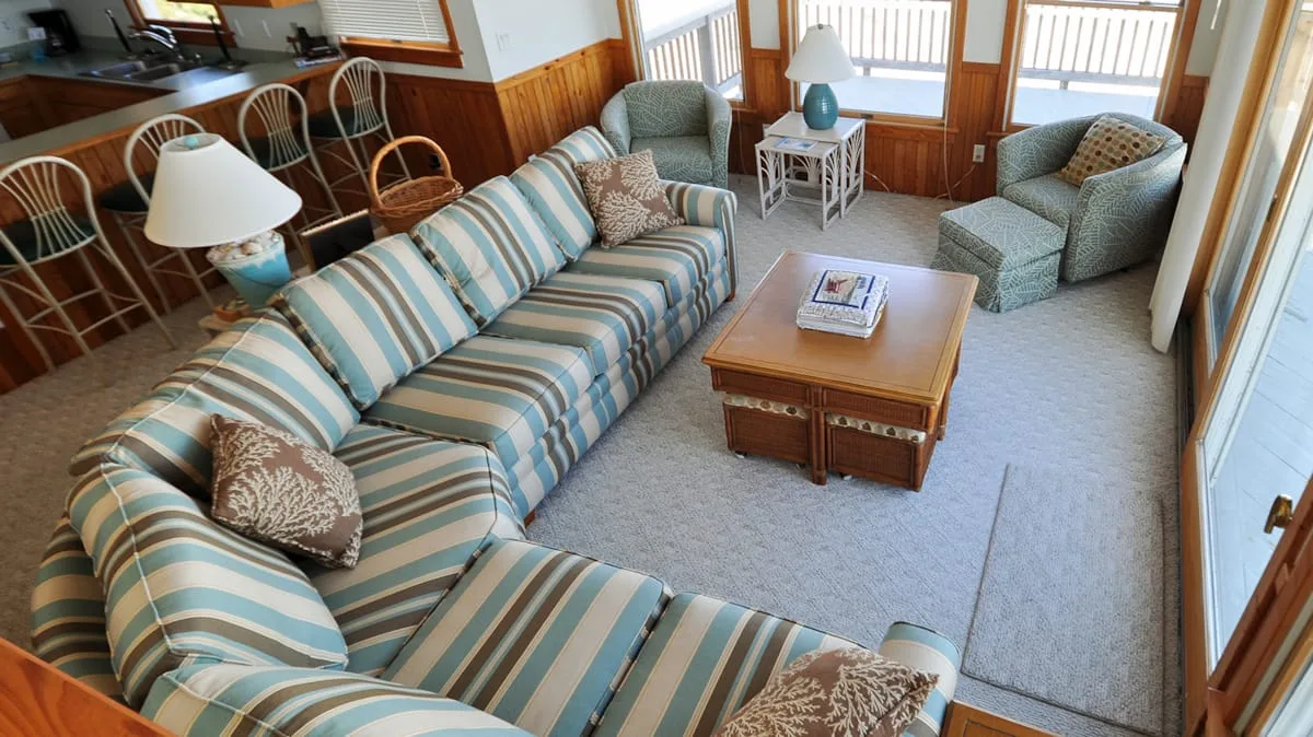 Una sala de estar con asientos a rayas, una mesa de centro y ventanas grandes.