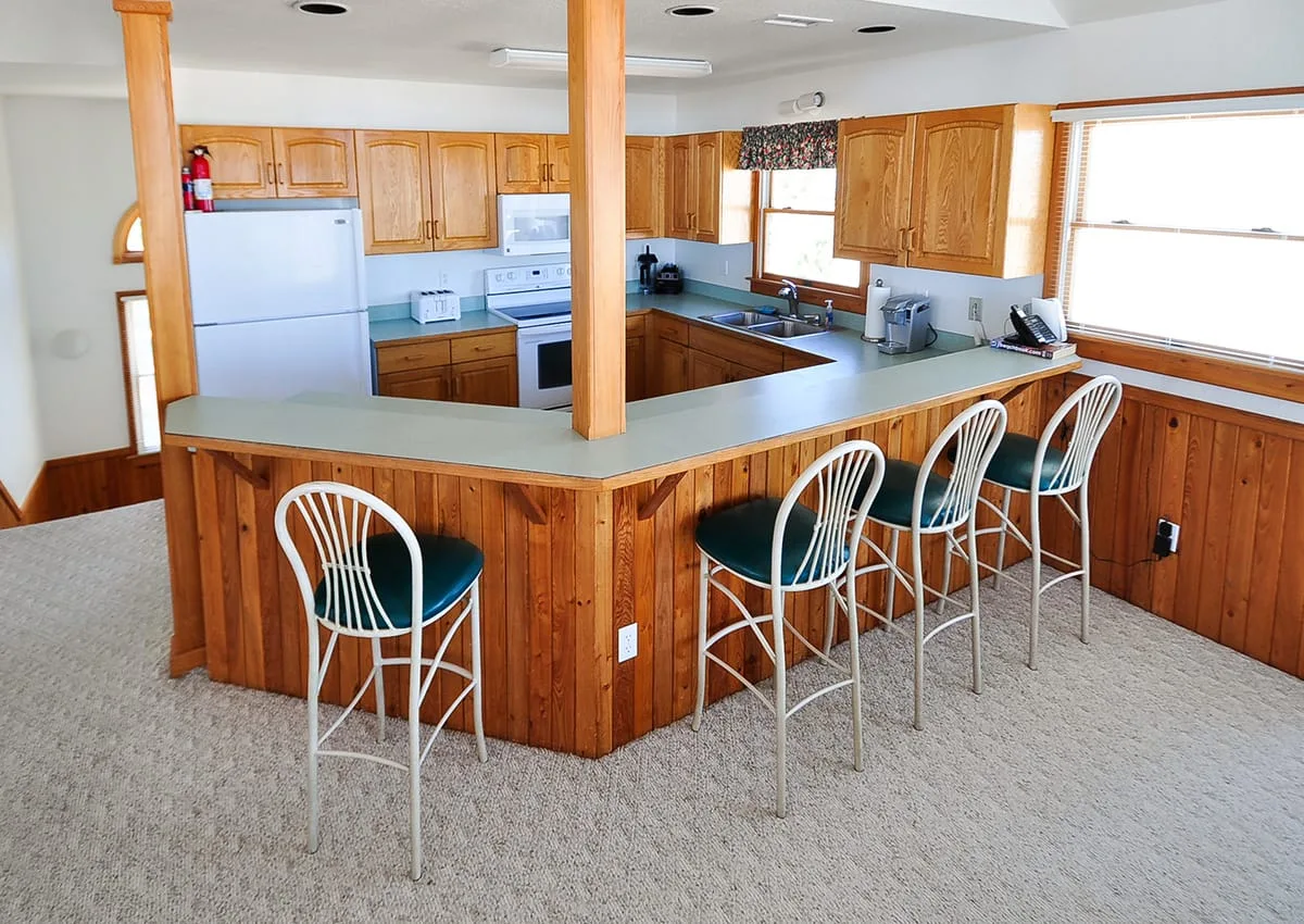 A kitchen with a long counter, wooden cabinets, and bar stools.