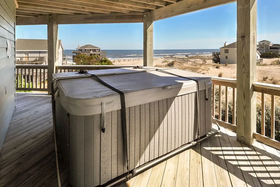 A hot tub sits on a covered wooden deck overlooking the beach.