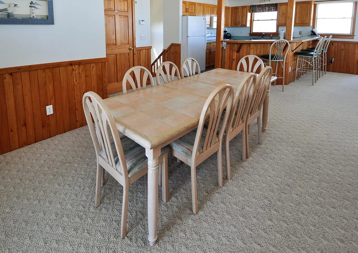 A dining area with a long table and chairs beside an open kitchen.