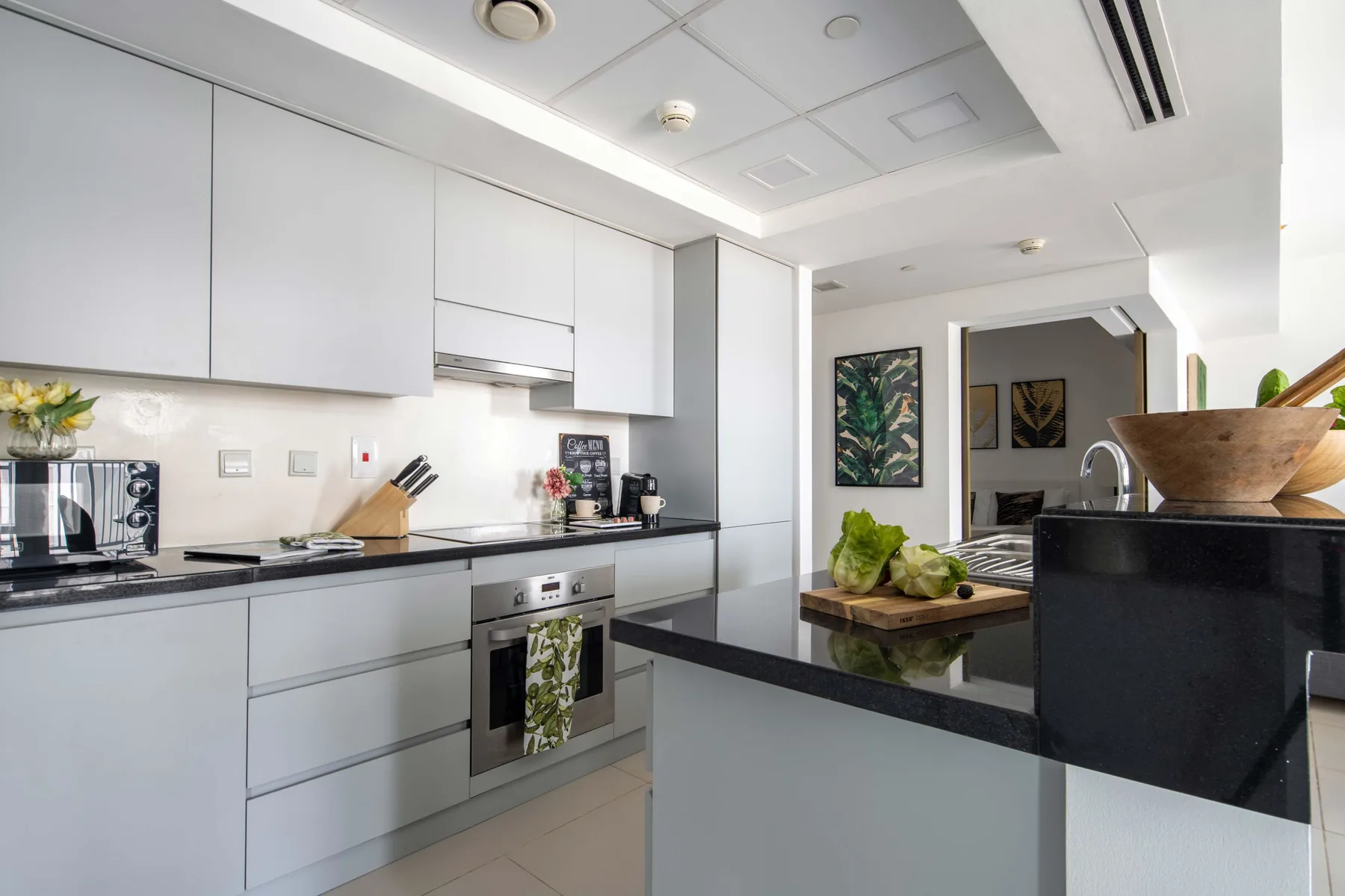 Una cocina moderna con gabinetes blancos, encimeras oscuras y un comedor al fondo.