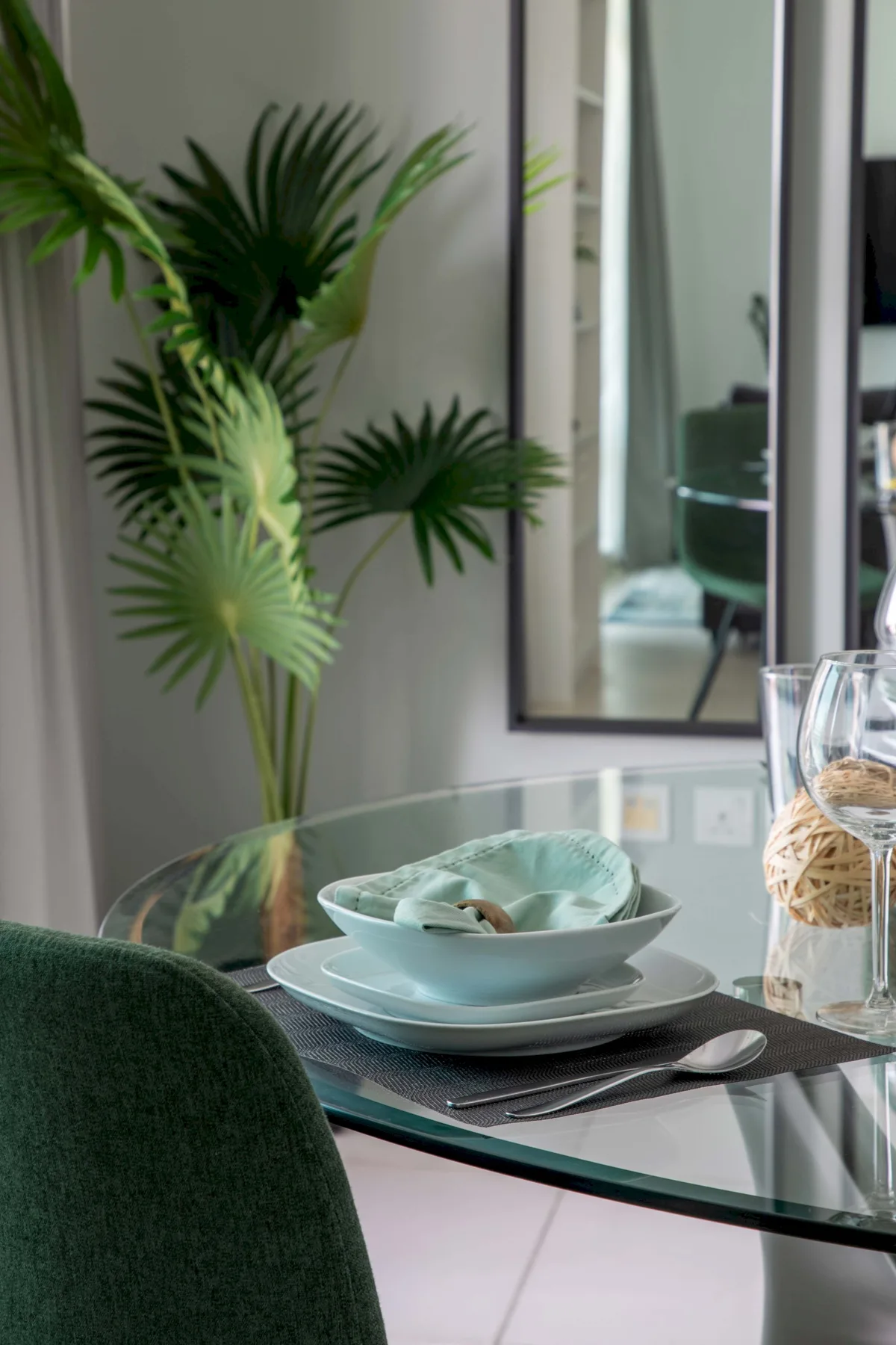 Comedor con una mesa de vidrio puesta con platos junto a una planta frondosa.