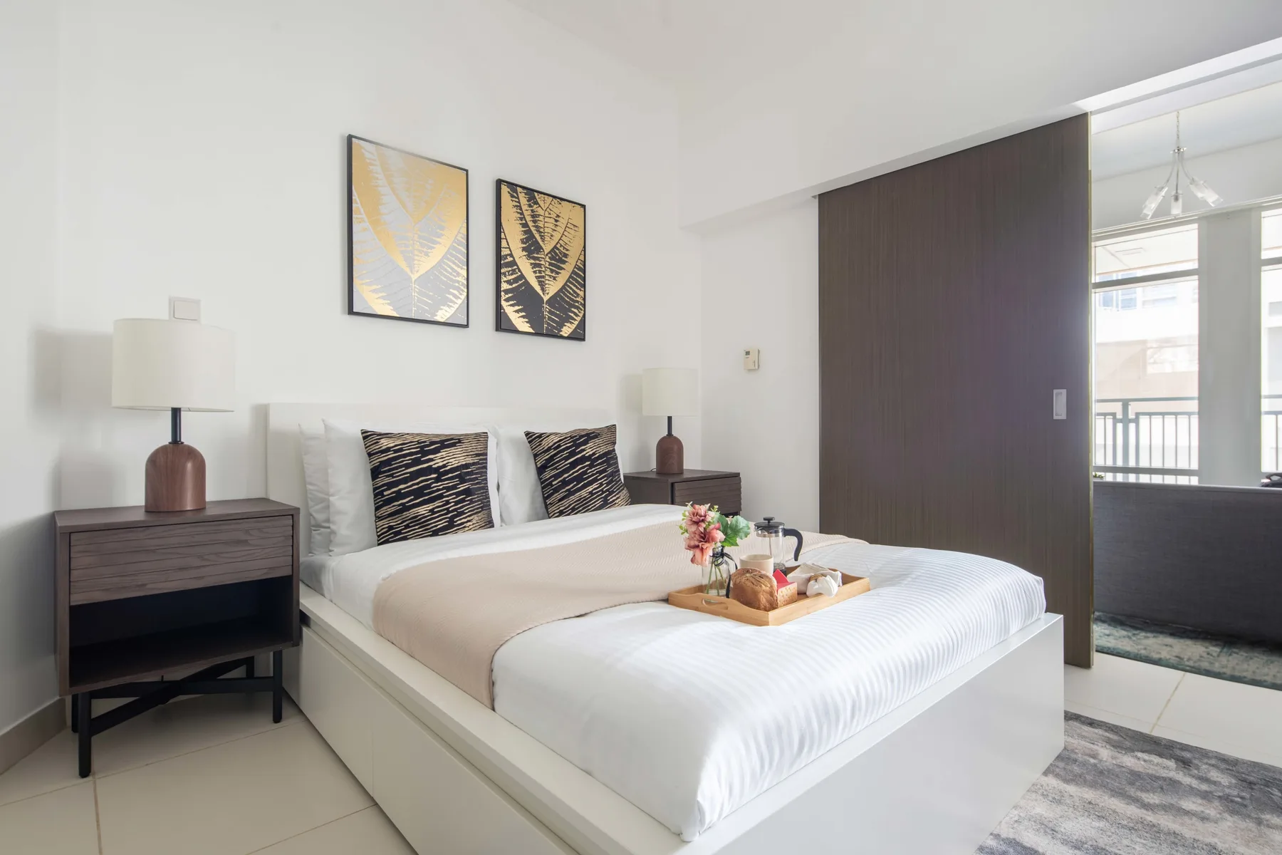 Un dormitorio luminoso con una cama bien tendida y cuadros enmarcados encima.