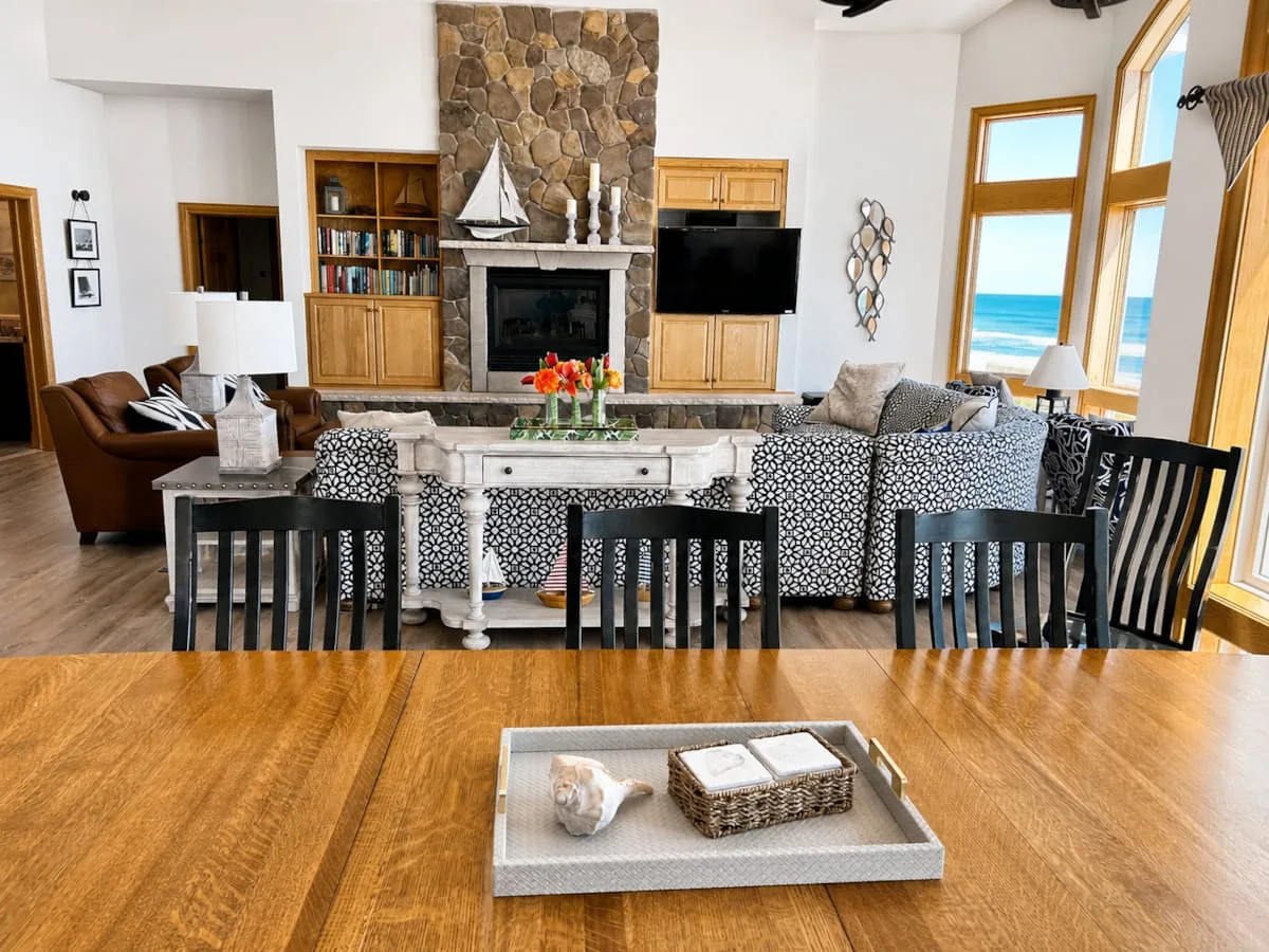 Una sala de estar con asientos estampados, una chimenea de piedra y vistas al mar por ventanas altas.