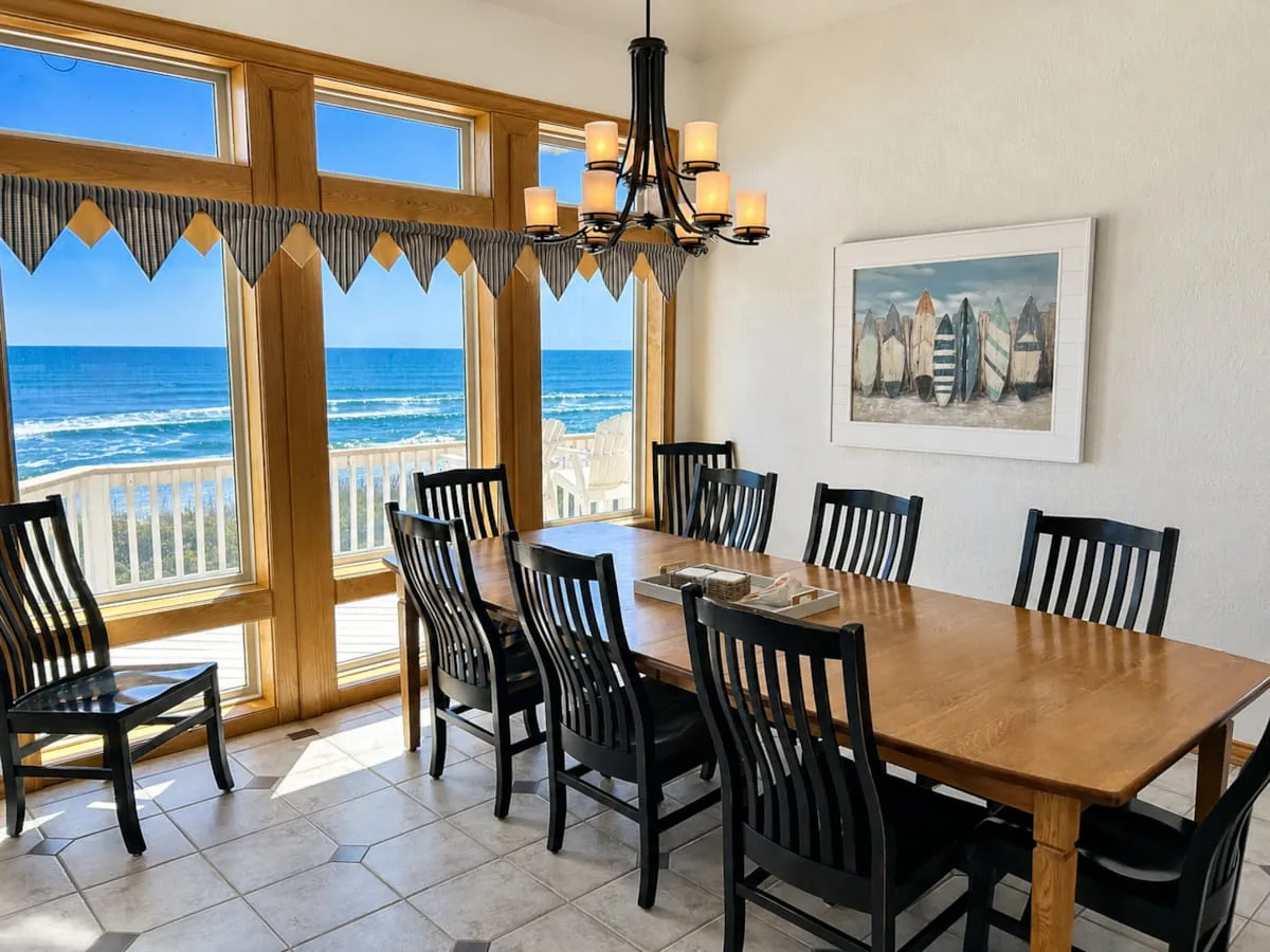 Comedor con mesa de madera y vistas al mar a través de grandes ventanas.