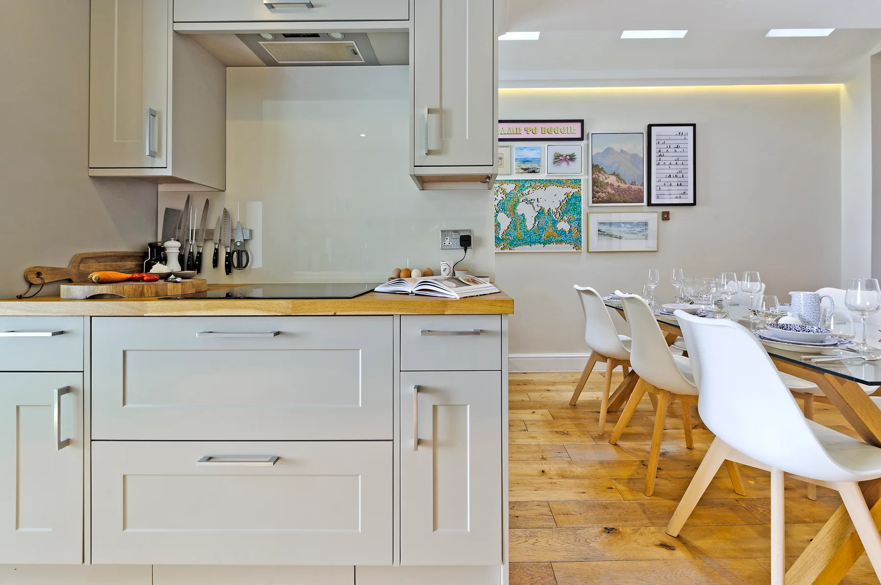 A modern kitchen opens onto a dining area with a long table and white seating.