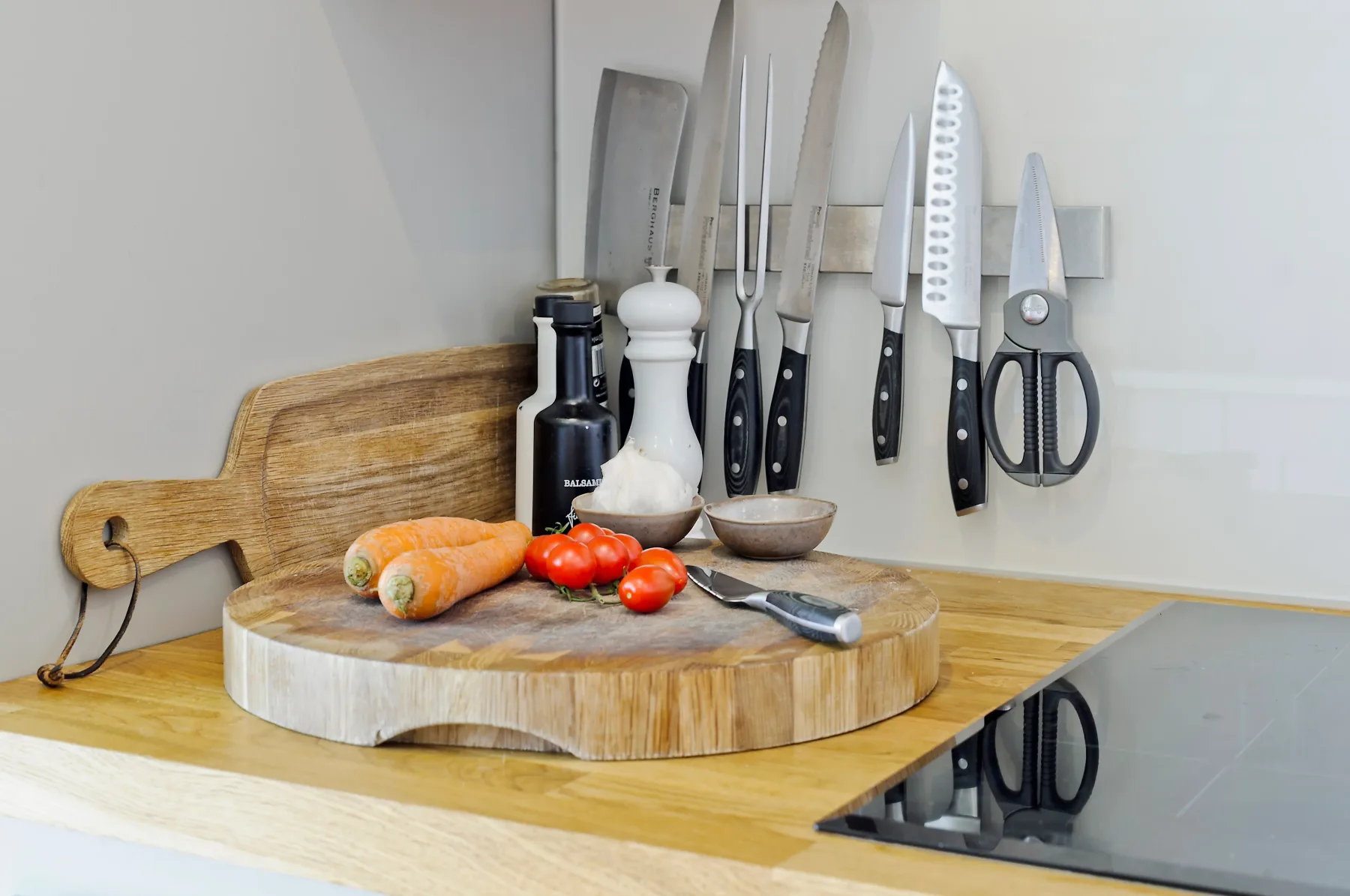 Una encimera de cocina muestra verduras, una tabla de cortar y cuchillos colgados.