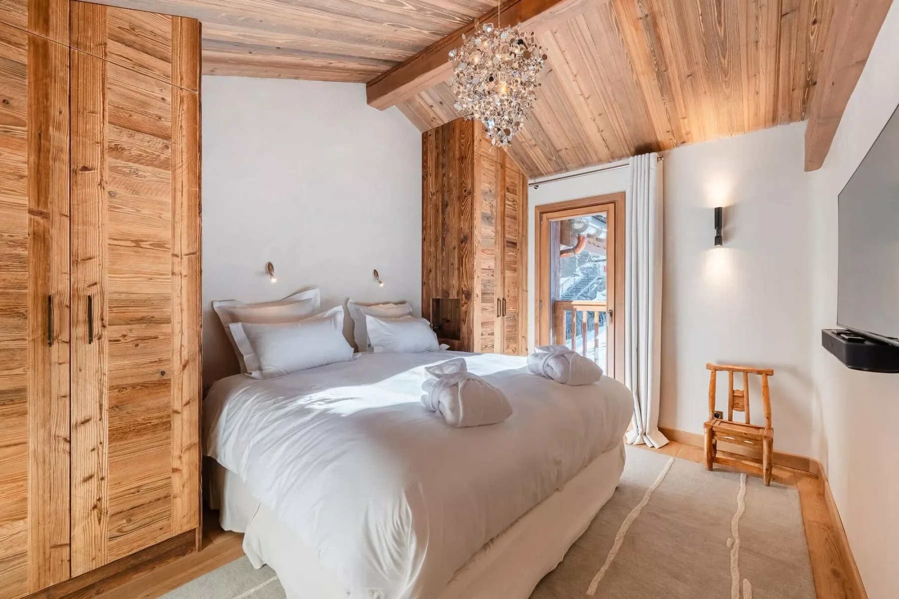 Un dormitorio con una cama, techo revestido de madera y una puerta de vidrio.