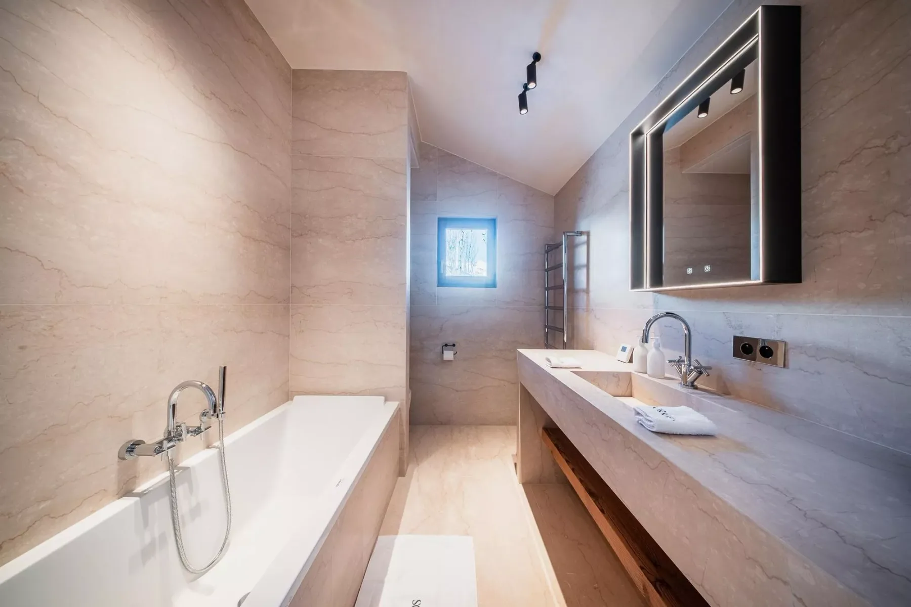 Un baño amplio con bañera, un largo lavabo y una ventana al fondo.