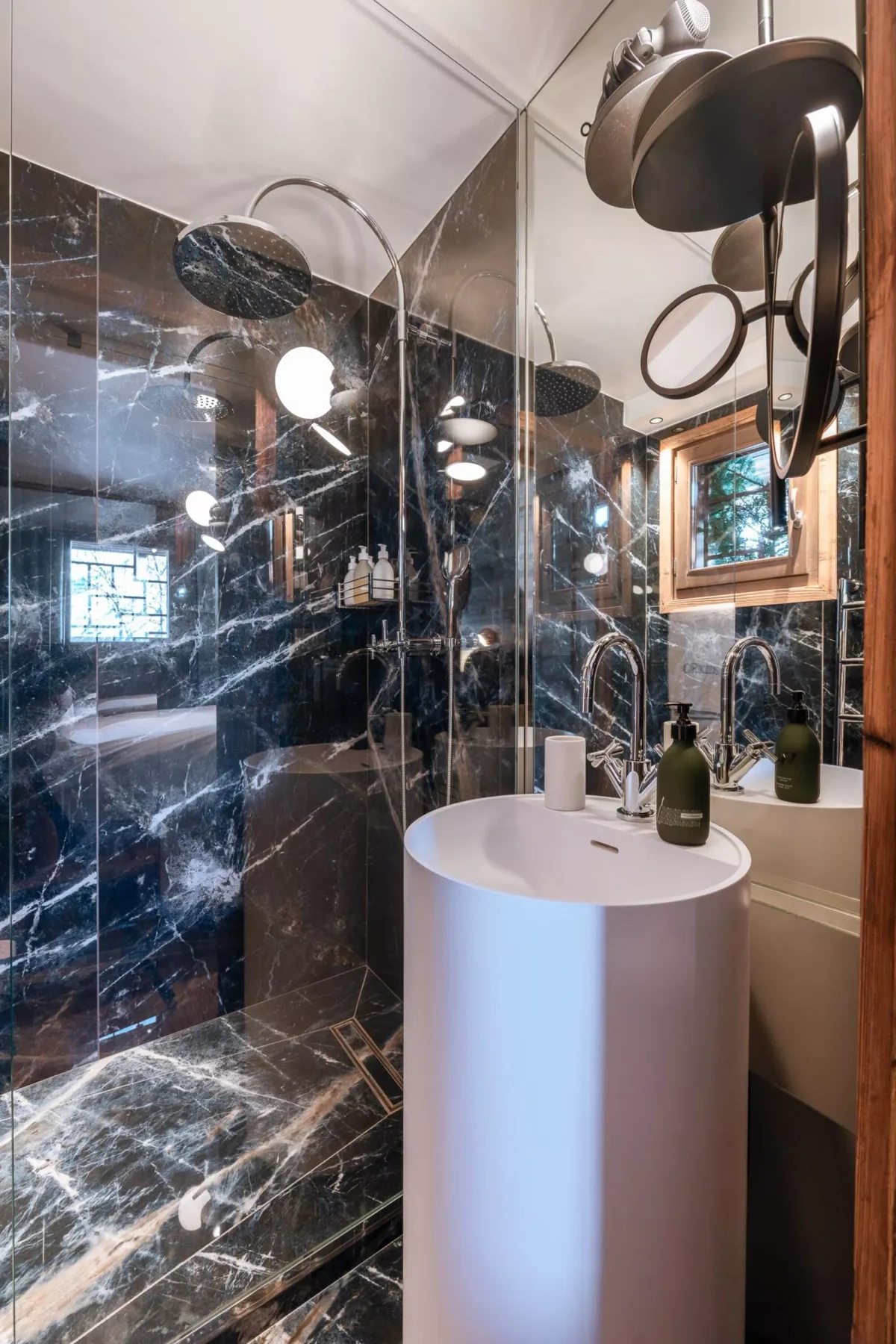 Un baño con azulejos oscuros veteados, un lavabo exento y una ducha de lluvia.