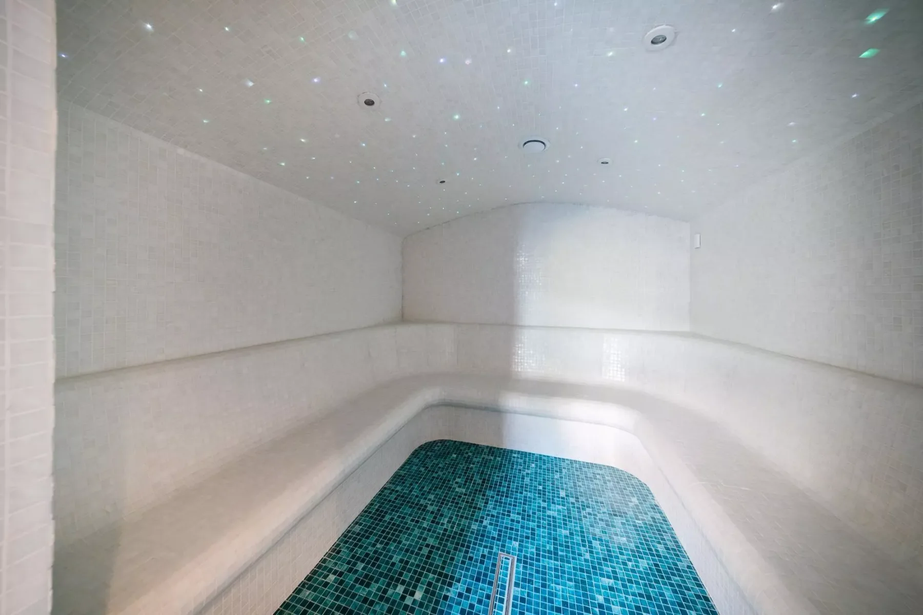 Una pequeña piscina interior con mosaicos azules queda bajo un techo suavemente iluminado.