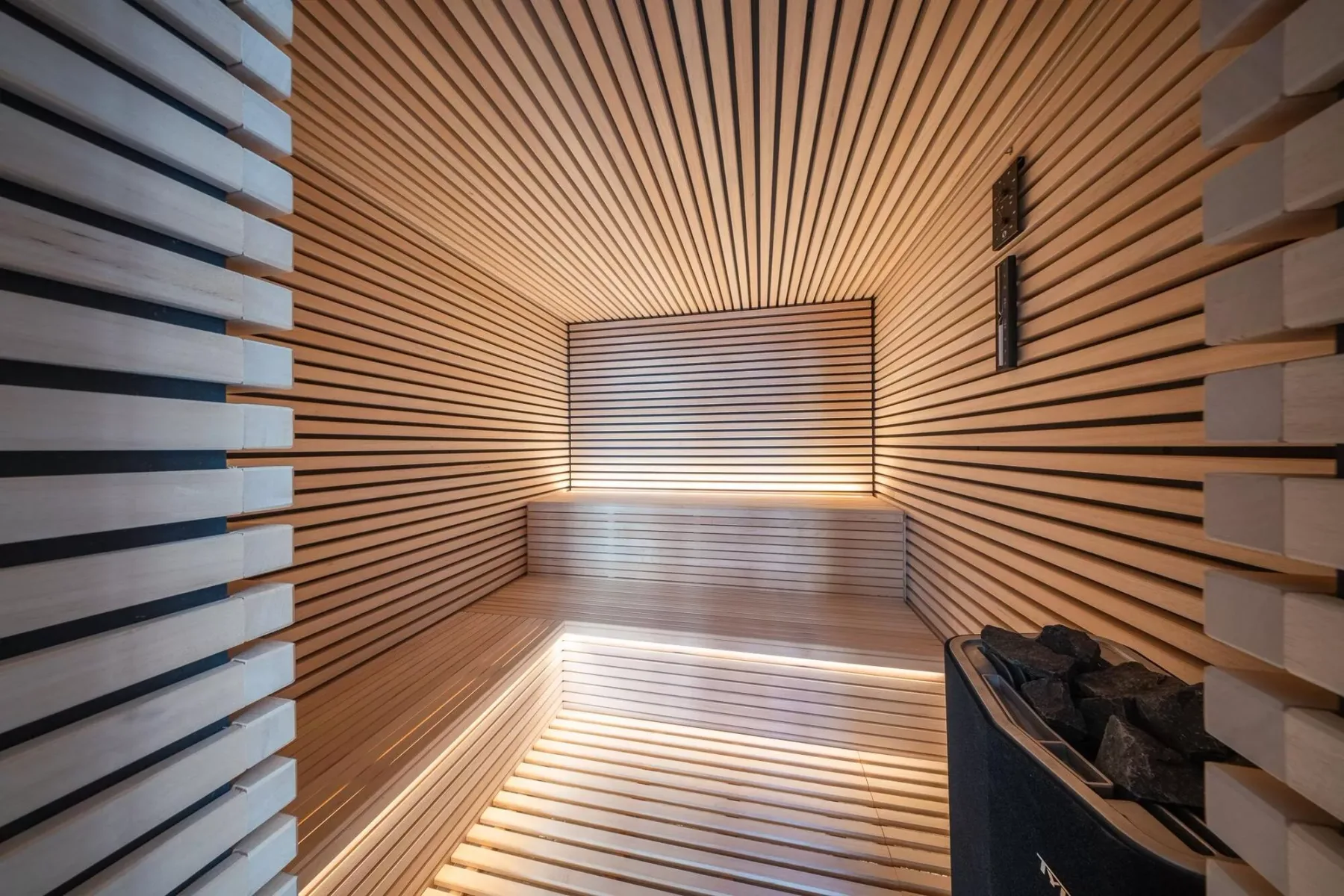 Una sauna revestida de madera, con asientos escalonados y un calentador con piedras.