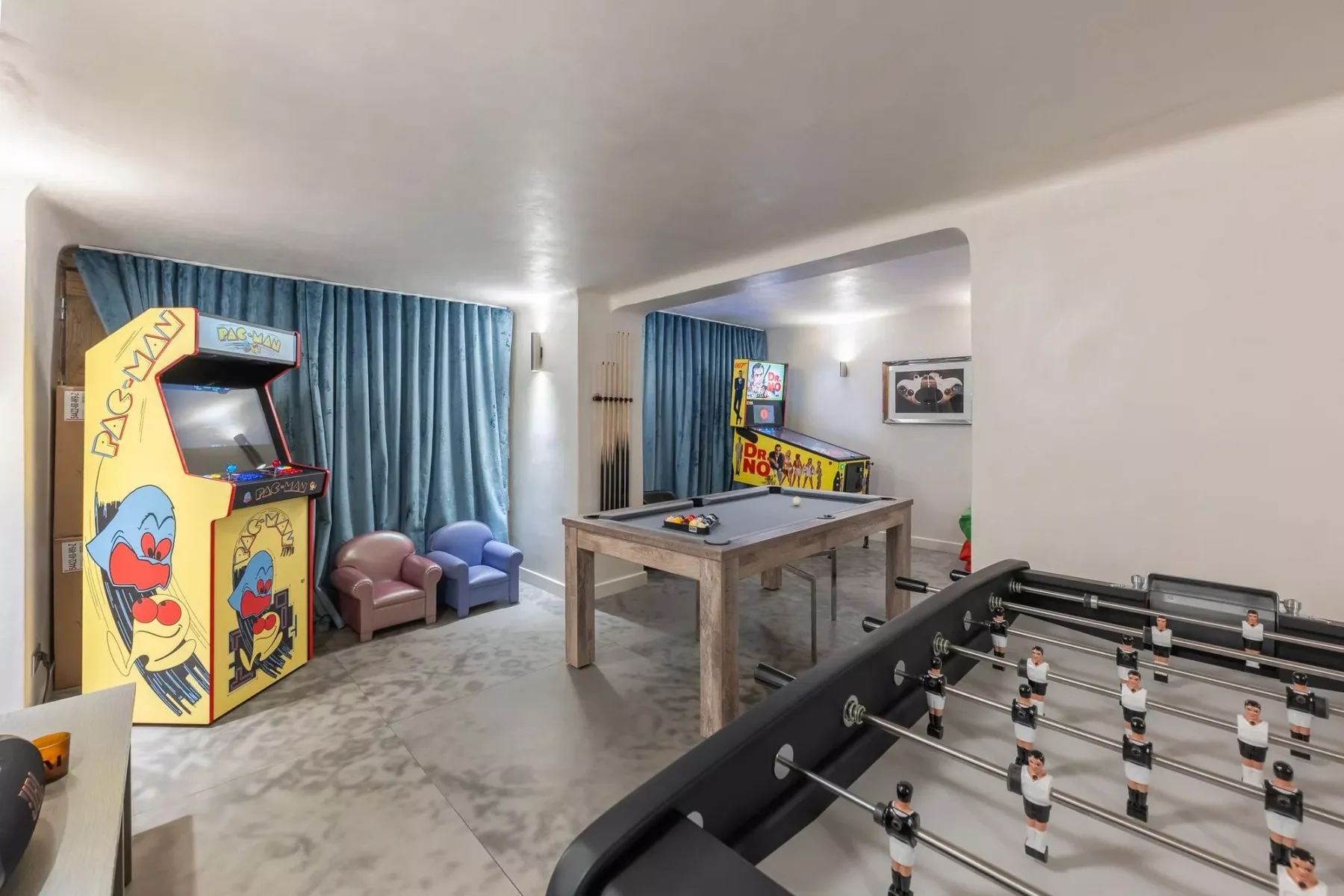 Una sala de juegos con una máquina recreativa, futbolín y asientos.