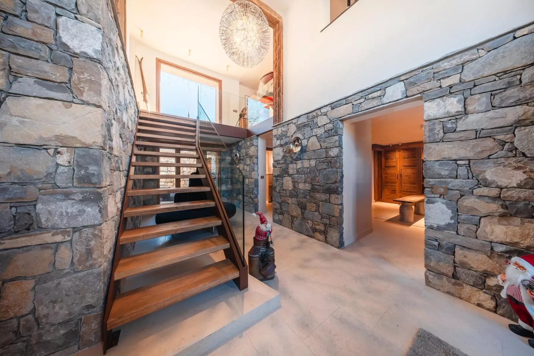 Un recibidor con paredes de piedra tiene una escalera de madera abierta y una puerta a otra habitación.