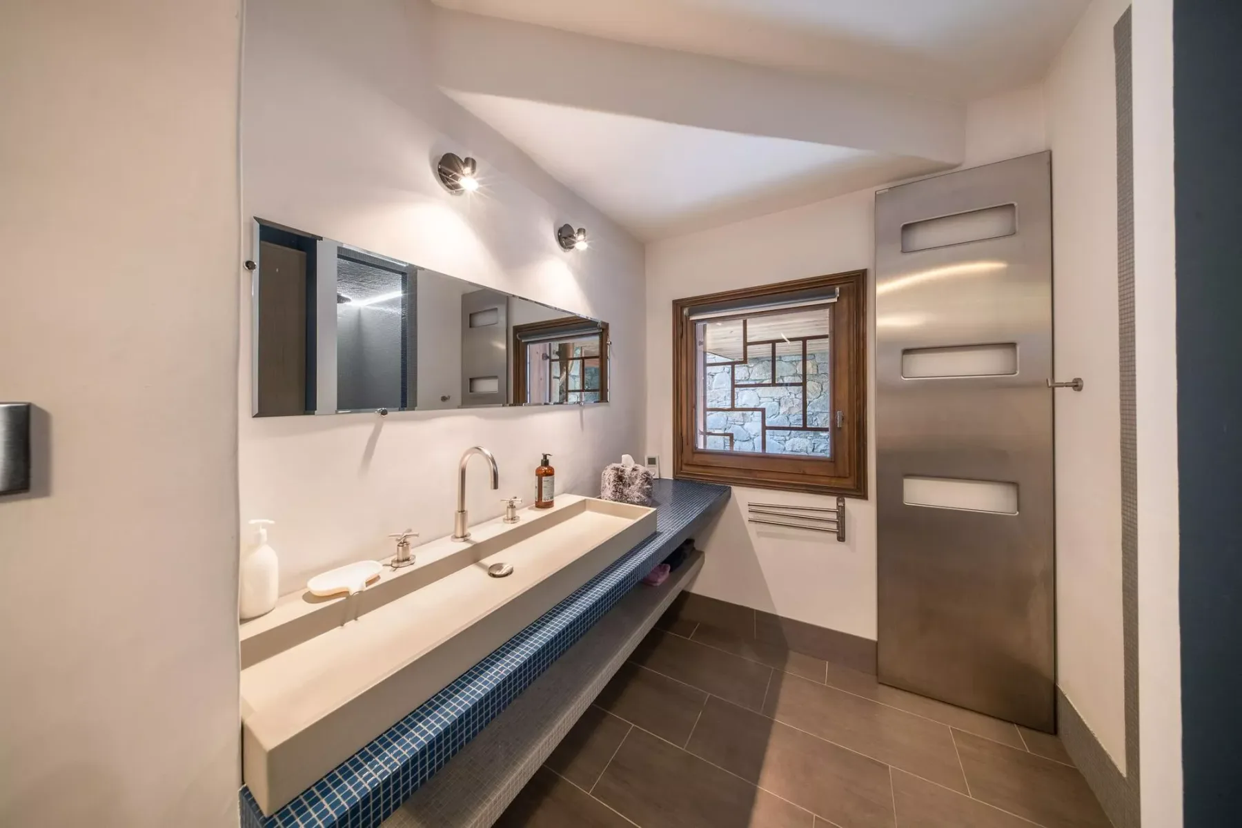 Un baño con una encimera larga con lavabo, espejos de pared y una ventana.