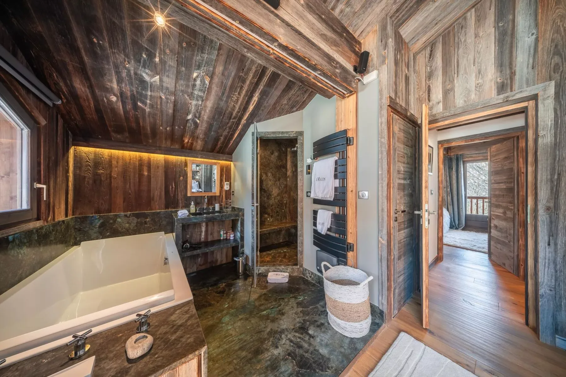 Un baño rústico con bañera, lavabo y una puerta hacia una habitación contigua.