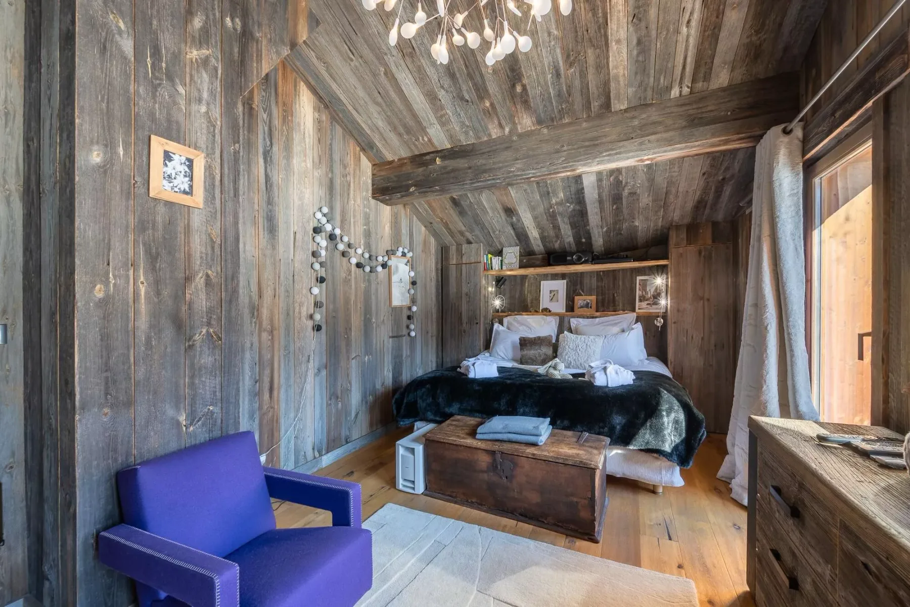Un dormitorio rústico con una cama, paredes de madera y un sillón morado.