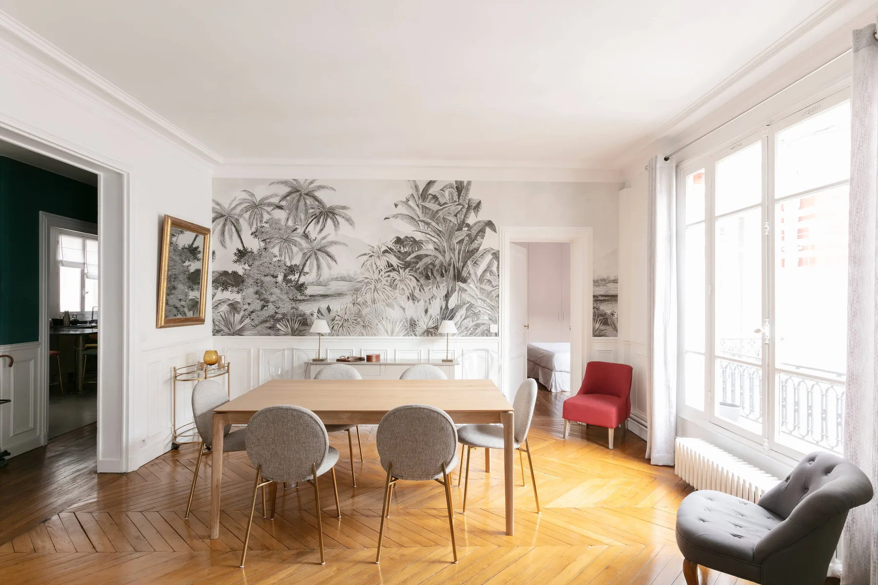 Un comedor luminoso con una mesa de madera, asientos tapizados y grandes ventanales.