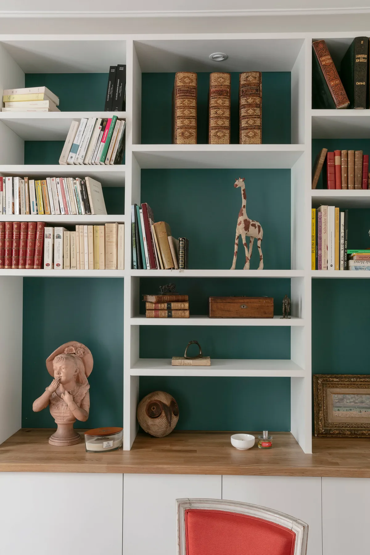 Una librería empotrada exhibe libros y objetos decorativos en estantes verde oscuro.