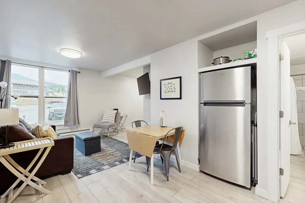 A bright living and dining area with a table, seating, and large windows.