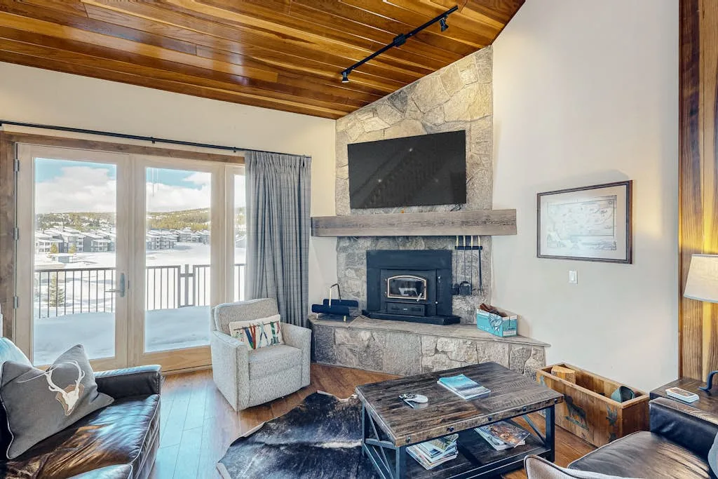 A living room with a stone fireplace, television, and glass doors opening onto a balcony.