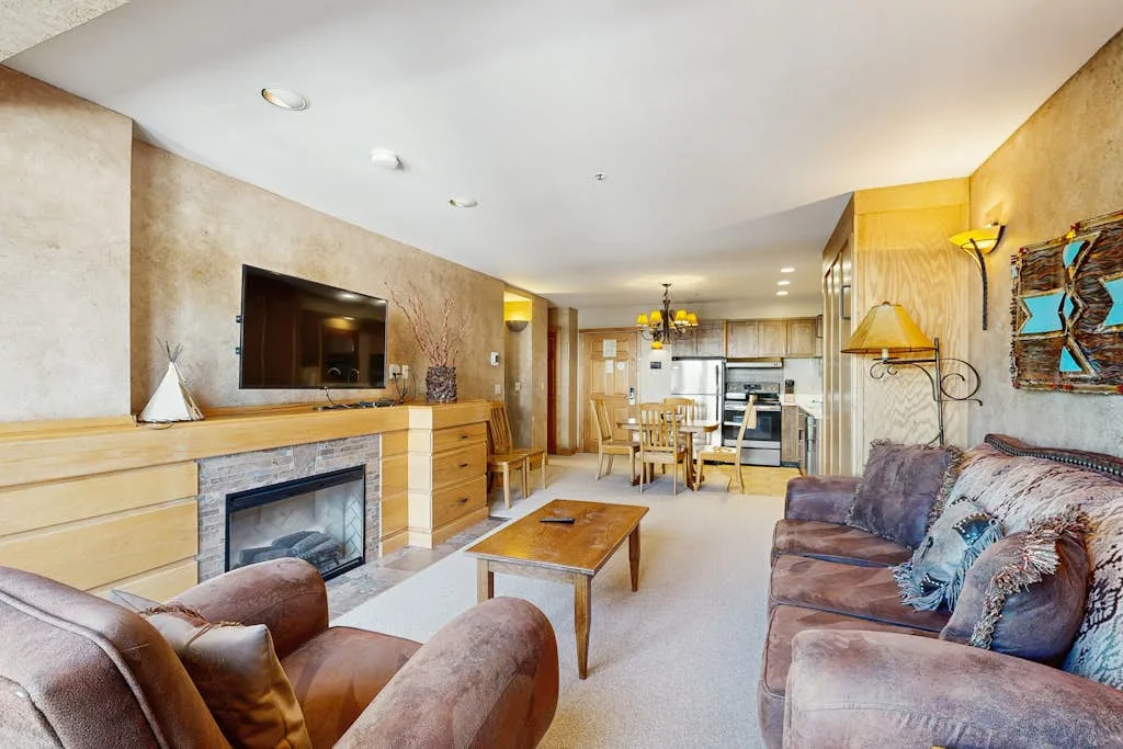 A living room with seating, a coffee table, and a kitchen visible beyond.