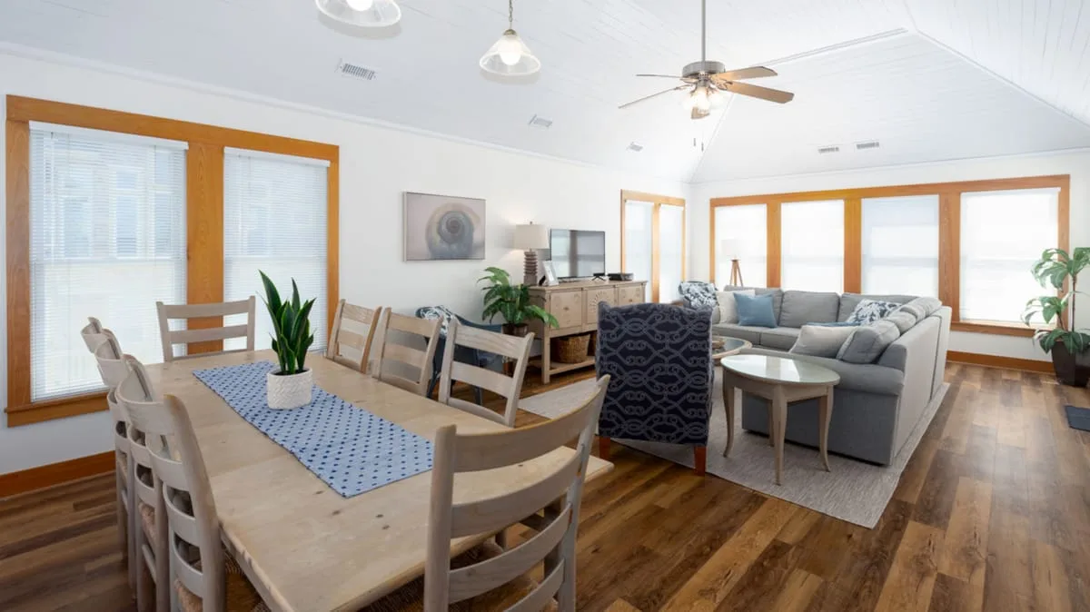 An open dining and living area with a dining table and seating by large windows.