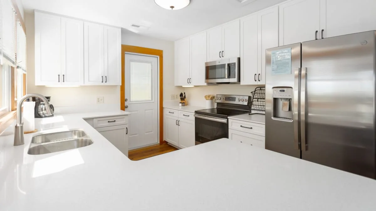 Una cocina luminosa con gabinetes blancos y electrodomésticos de acero inoxidable.