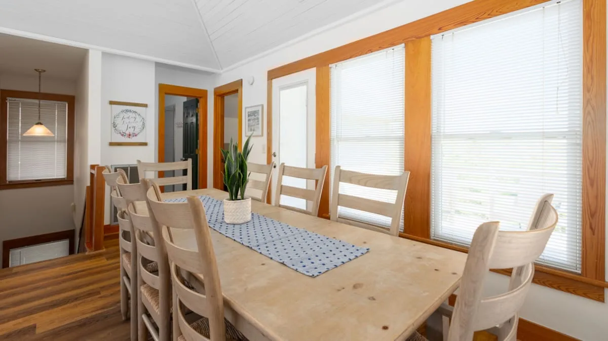 A dining area with a long wooden table and large windows.