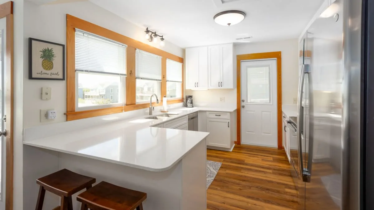 A bright kitchen with white cabinets, a peninsula, and wood-trimmed windows.