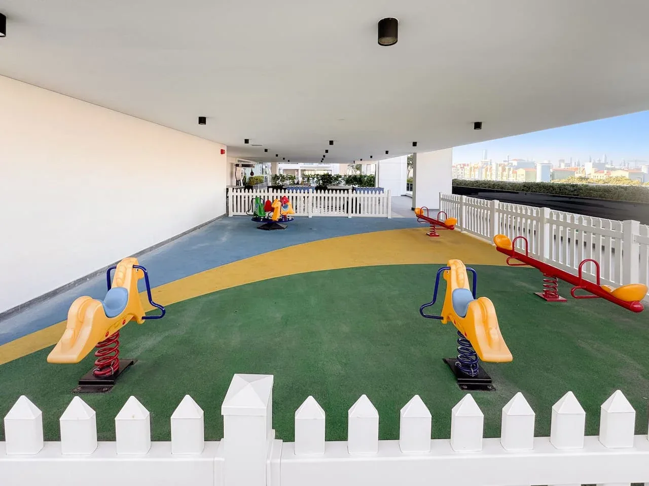 Un área de juegos infantil cubierta con equipos coloridos y una cerca blanca.