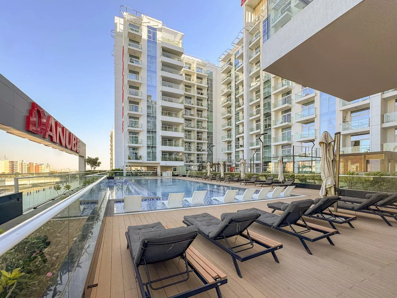 Una piscina al aire libre y una terraza están rodeadas de edificios de apartamentos modernos.